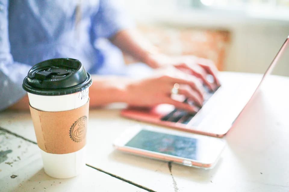 Une personne travaille sur un ordinateur portable, un gobelet de café posé à côté